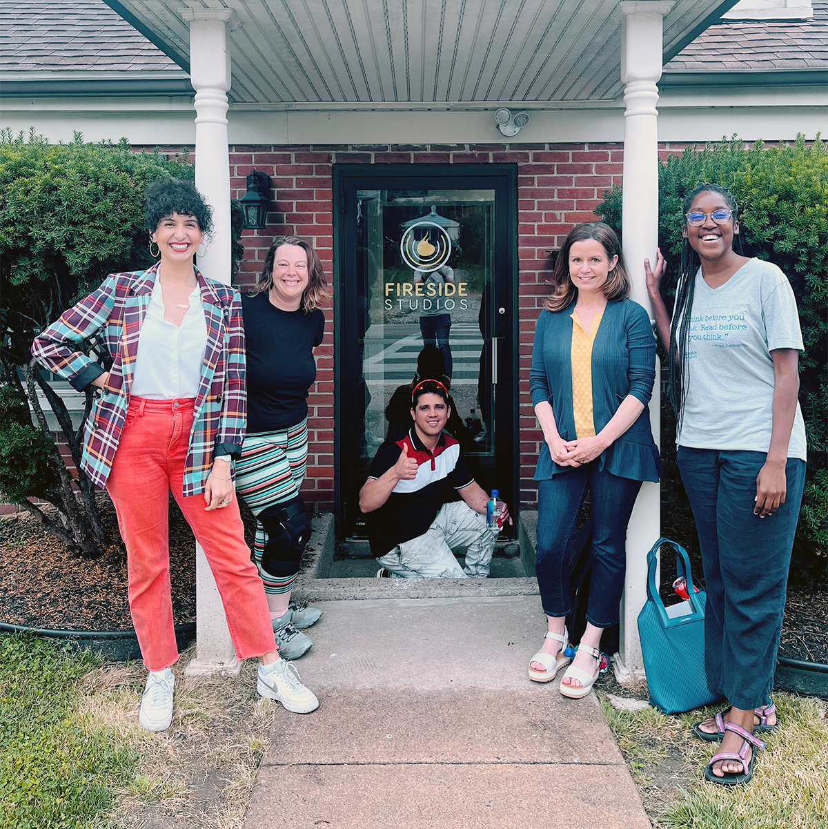 A group of four women and one man posing in front of a door to a studio.