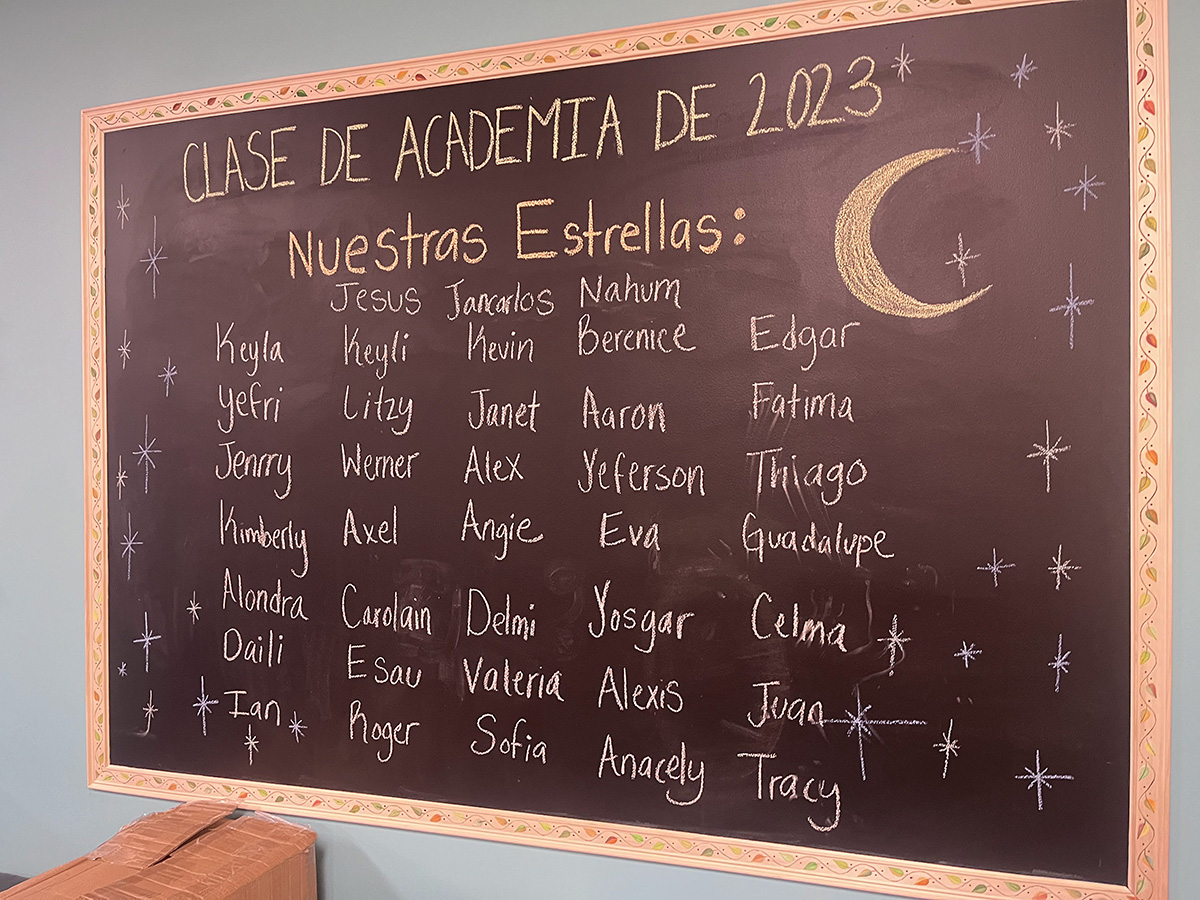 Chalkboard that says "Clase de academia de 2023" and lists childrens' names.